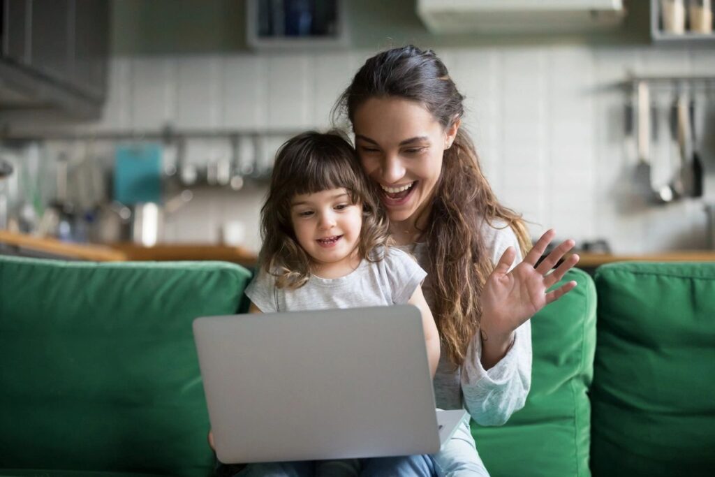 Working motherhood and mental health - a mom holds her daughter and waves to someone on the computer.